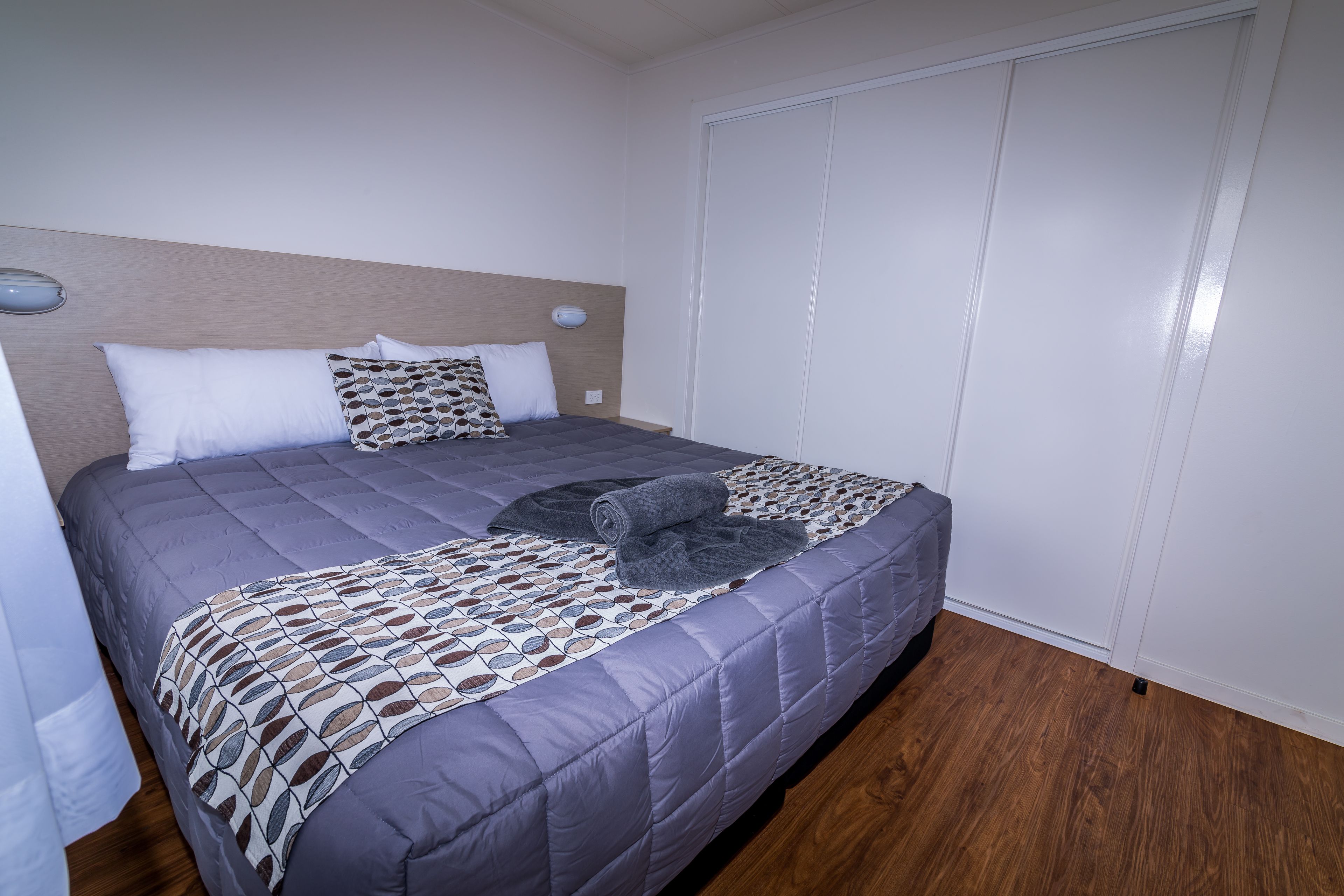A neatly made bed with a patterned bedspread, two pillows, and a rolled-up blanket.