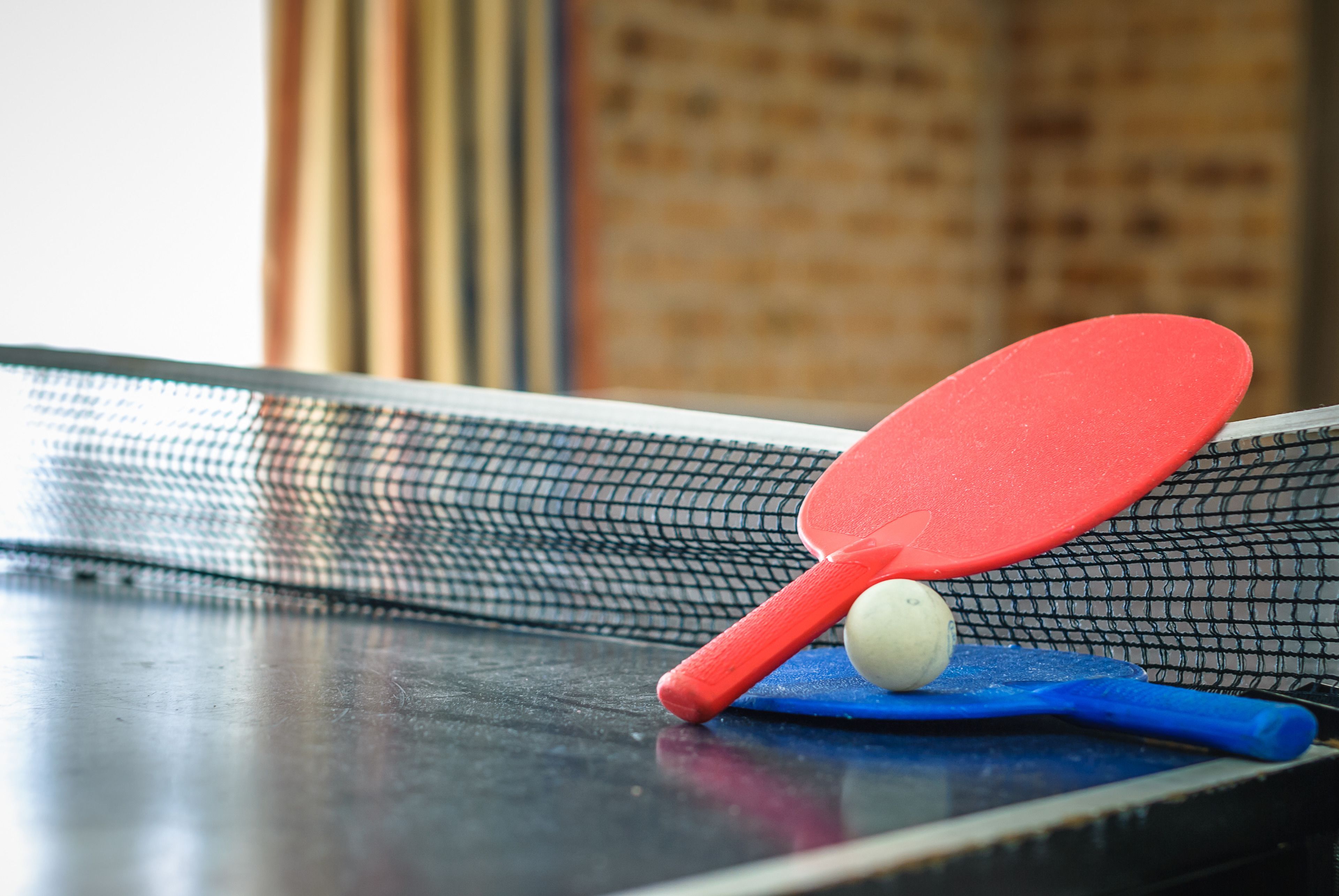 A table tennis table with a net, a red paddle, a blue paddle, and a white ball.