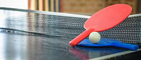 A table tennis table with a net, a red paddle, a blue paddle, and a white ball.