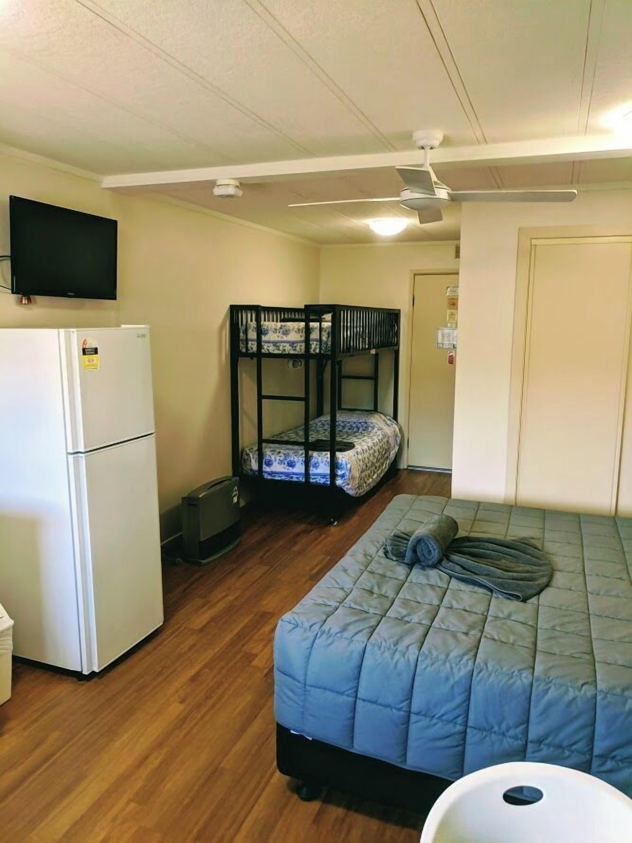 A compact room with bunk beds, a refrigerator, a television, and a ceiling fan.
