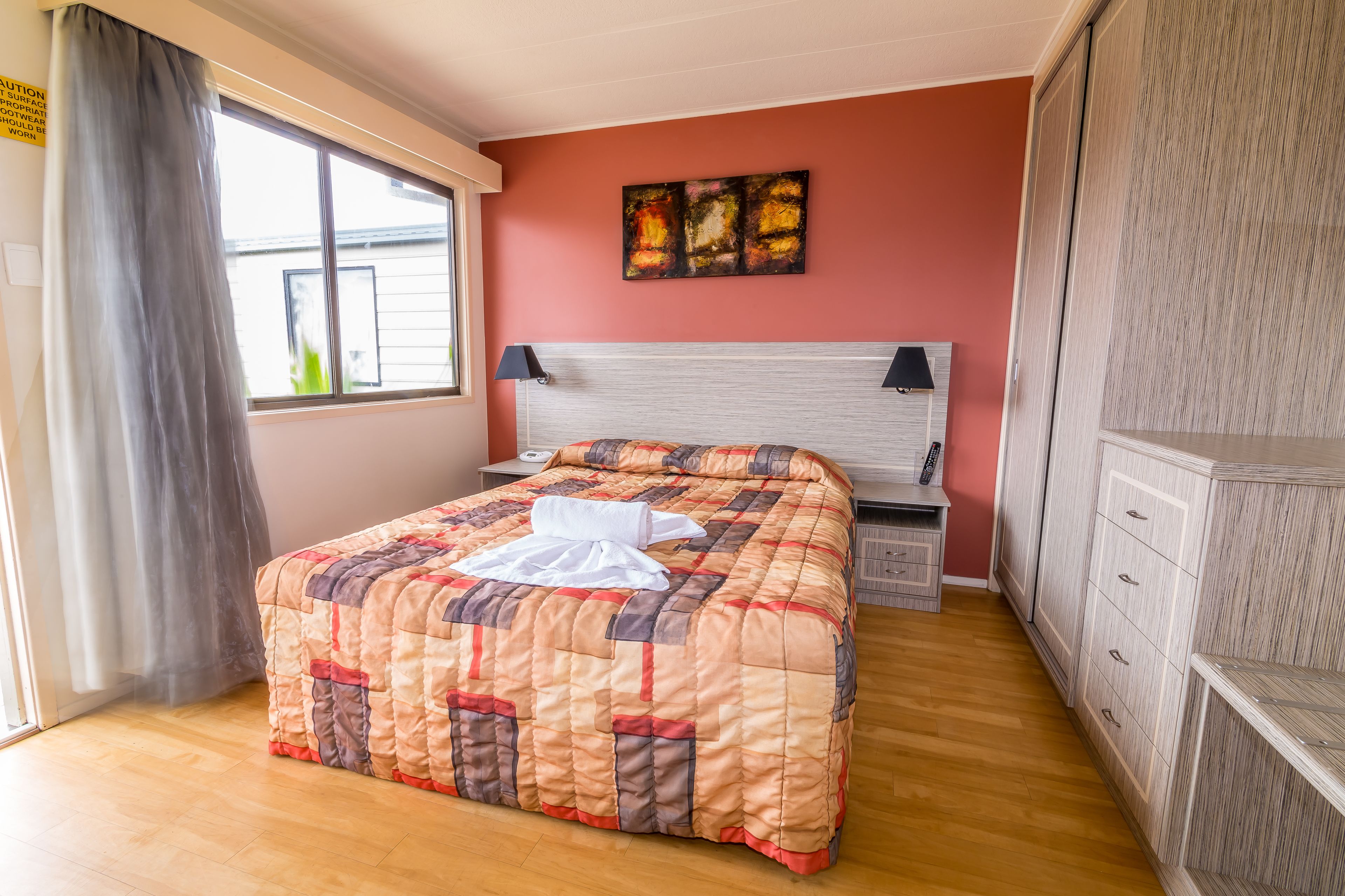Un lit bien fait, avec une couverture, une table de chevet avec une lampe, un tableau décoratif au mur et une armoire.