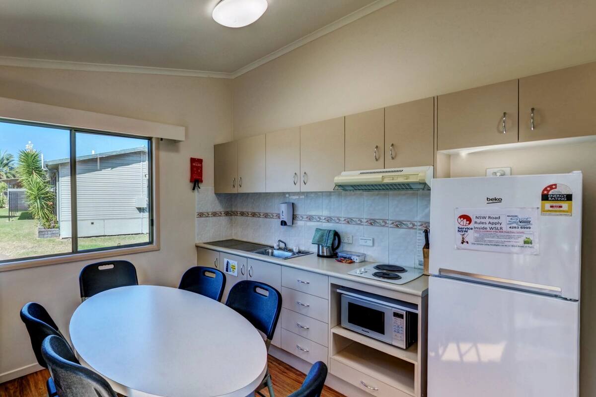 A compact kitchen with a dining table, chairs, a refrigerator, a microwave, and a window with curtains.