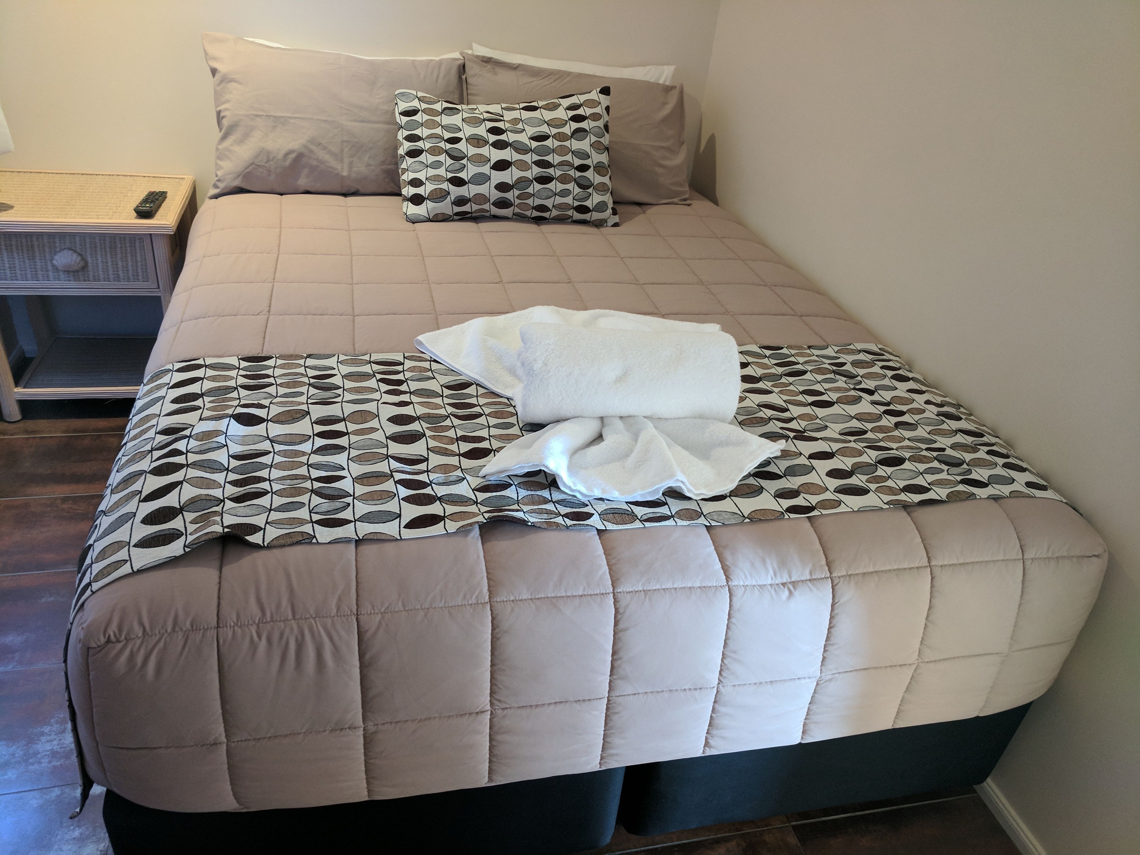 A neatly made bed with a patterned bedspread, two pillows, and a folded white towel.