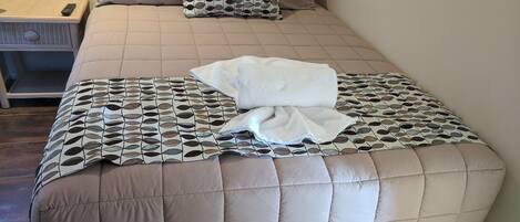 A neatly made bed with a patterned bedspread, two pillows, and a folded white towel.
