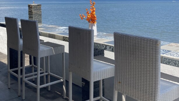 Una terraza con sillones de mimbre y un florero, con vista a un mar tranquilo.