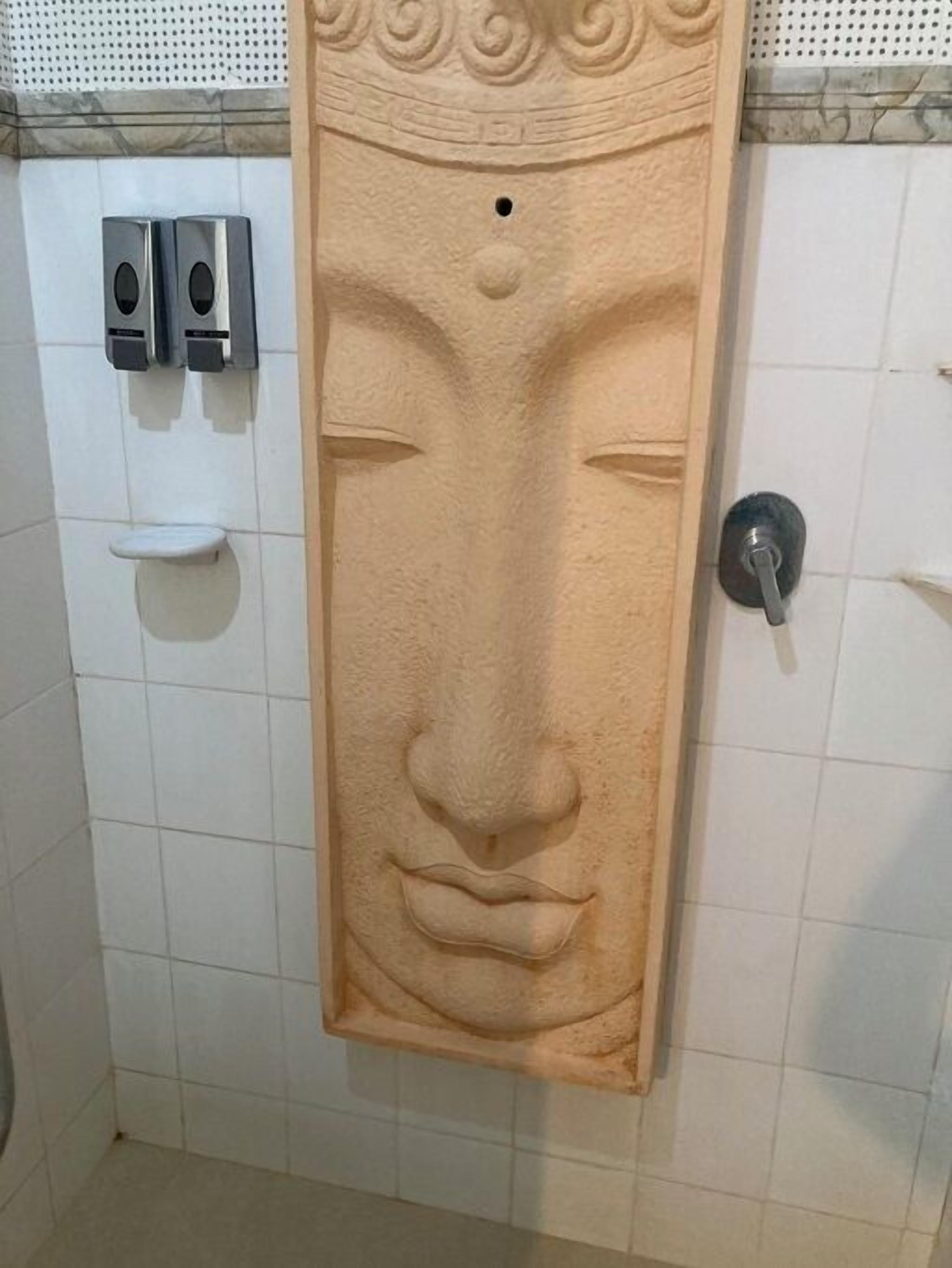 Een toiletruimte met een zeepdispenser aan de muur, een handdroger en een toilet.