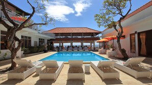 Zona de piscina con sillones, un área de estar techada y vista al mar.