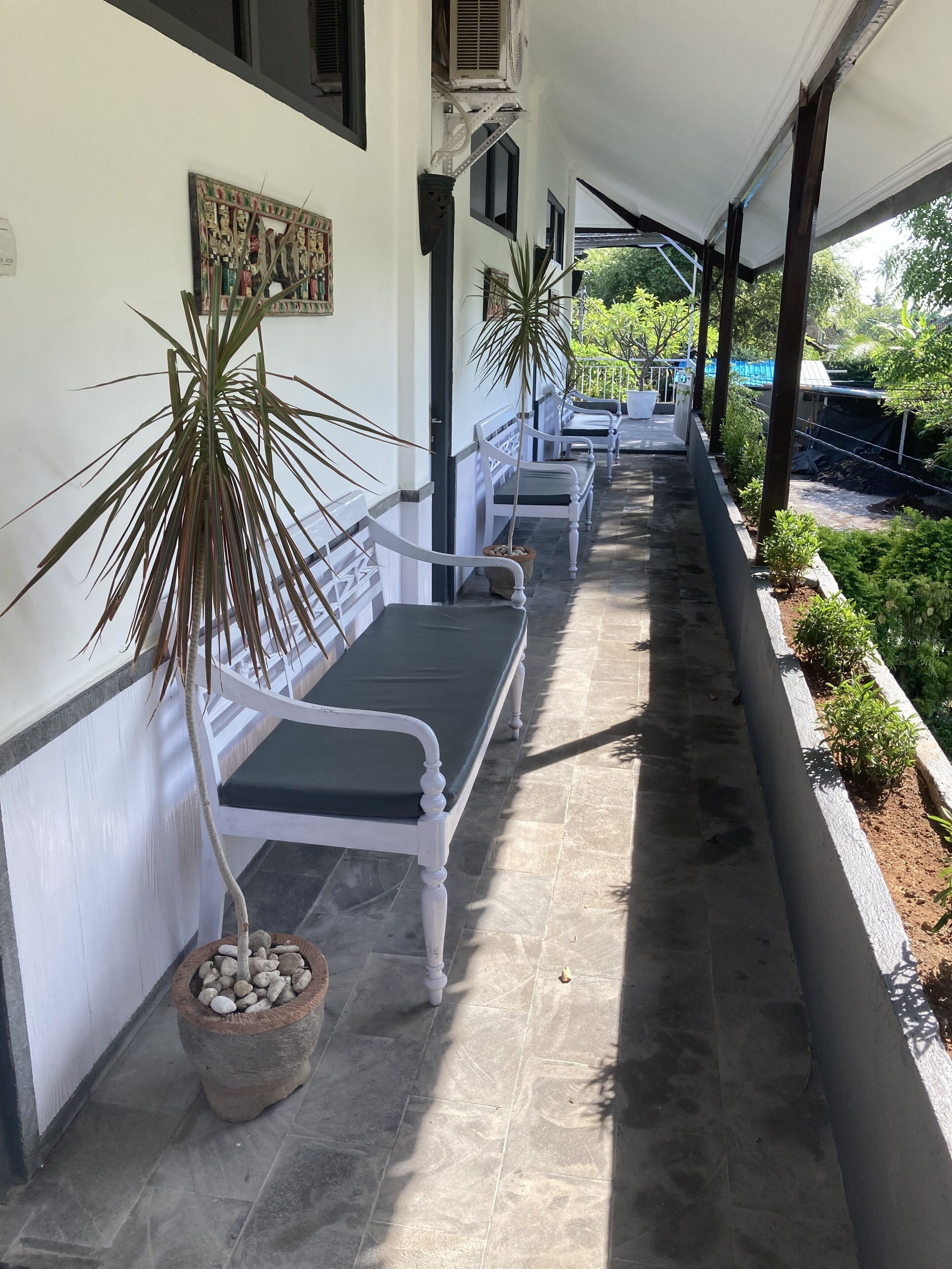 A covered outdoor seating area with white benches and potted plants.