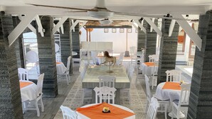 Un restaurante con mesas y sillas blancas, un ventilador de techo y vistas al mar.