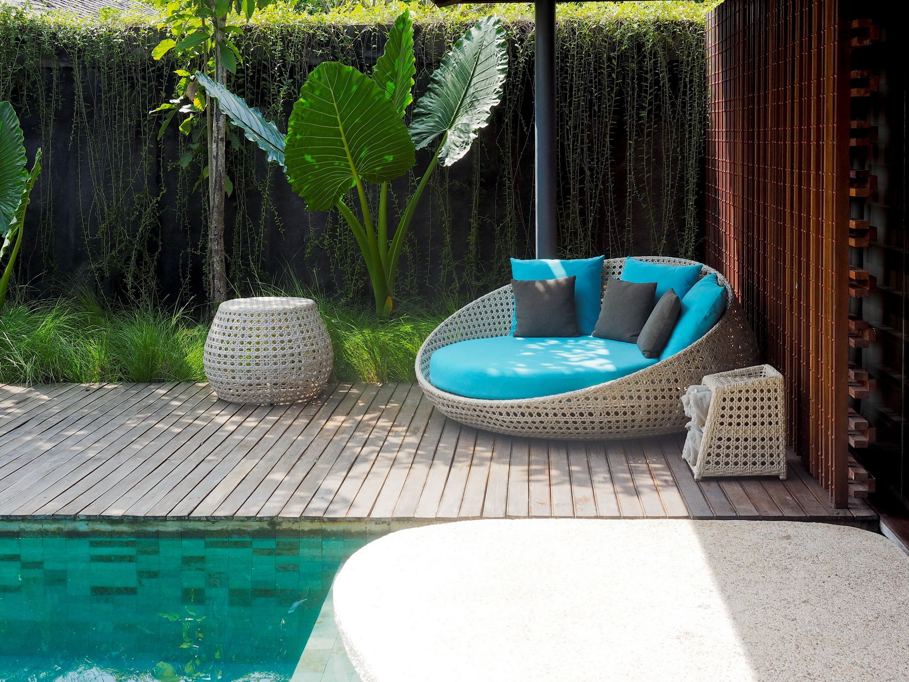A wicker outdoor seating area with cushions, a wooden deck, and a pool.