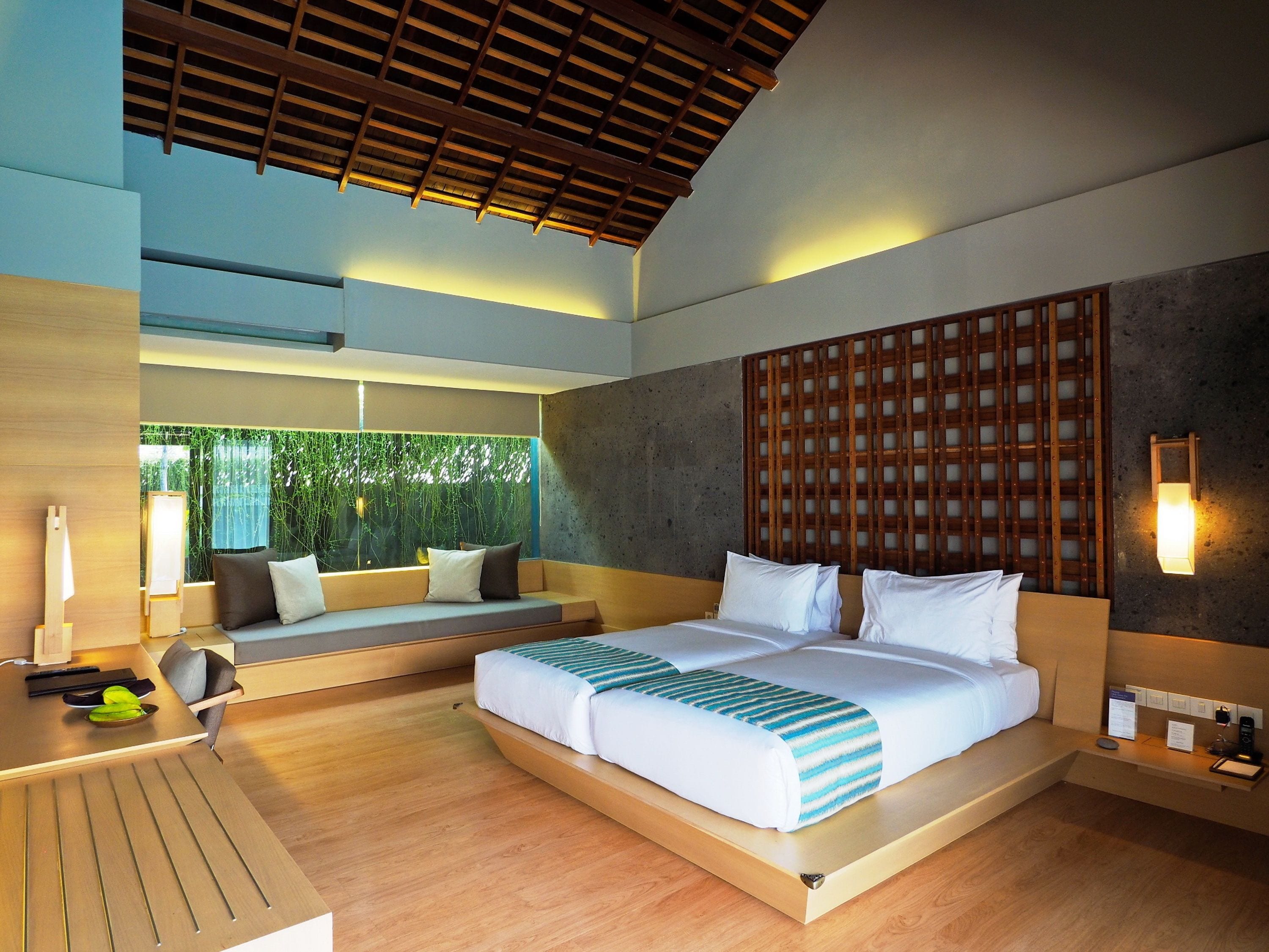 A modern hotel room with a large bed, a seating area, and a view of greenery outside.