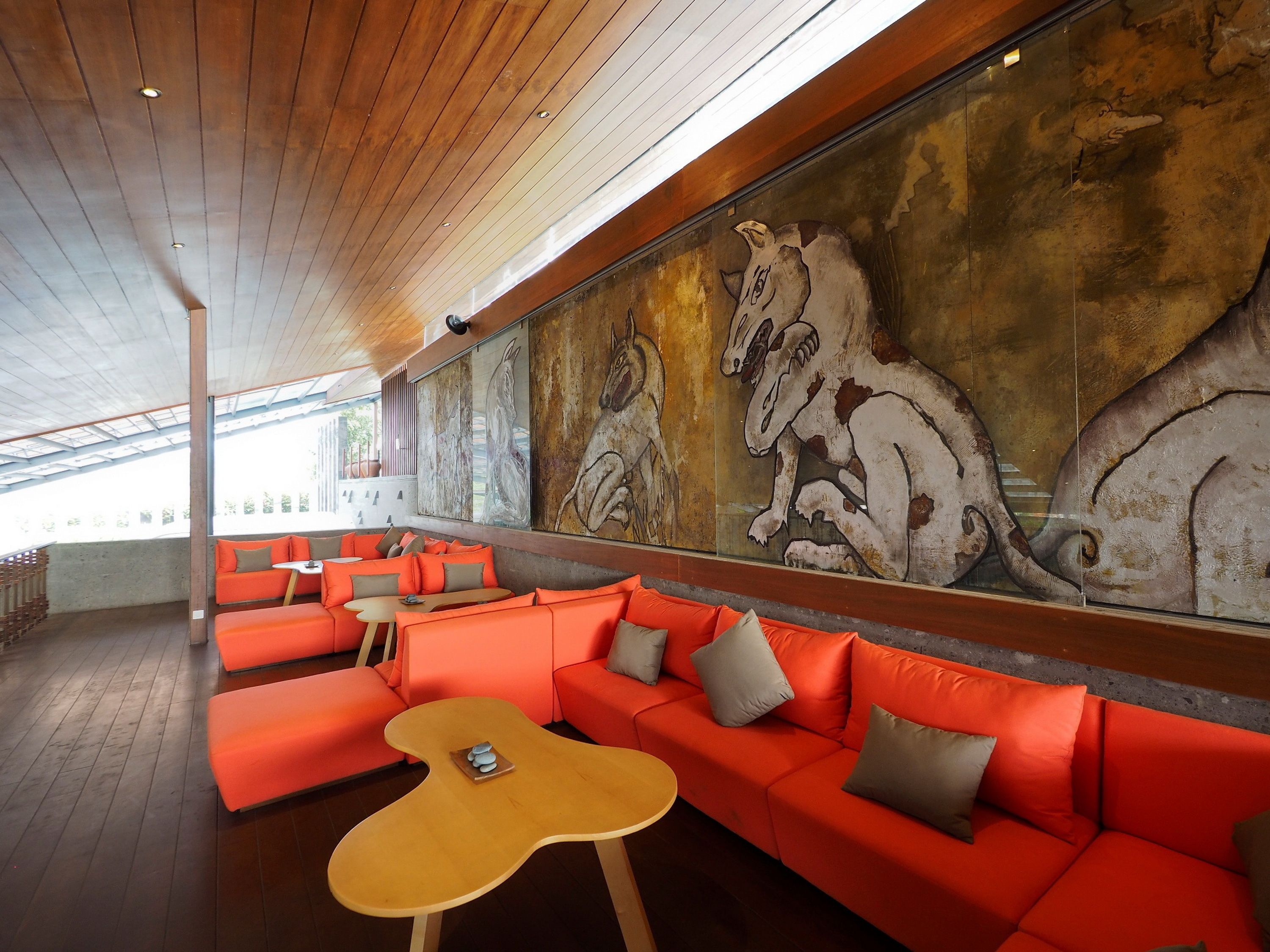 A modern lounge with orange seating, a large mural of horses, and a wooden ceiling.