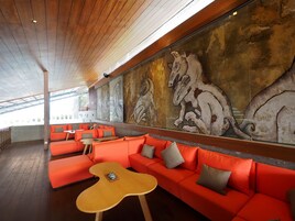 A modern lounge with orange seating, a large mural of horses, and a wooden ceiling.
