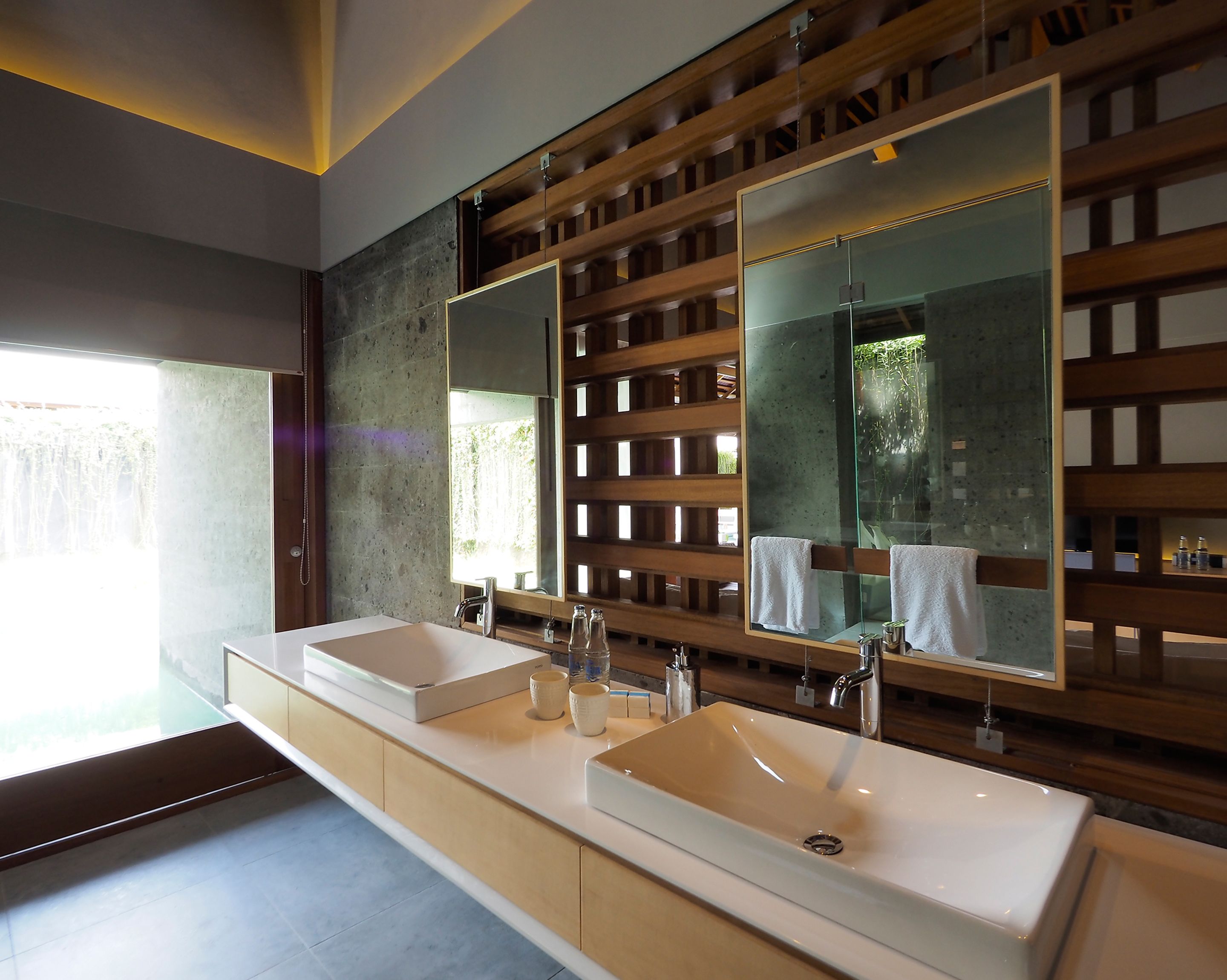 A modern bathroom with two sinks, a large mirror, and a wooden panel design.
