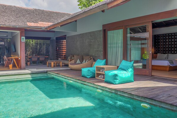 A poolside area with wooden decking, lounge chairs, and a glass-enclosed room. - The Santai by LifestyleRetreats (Kerobokan)