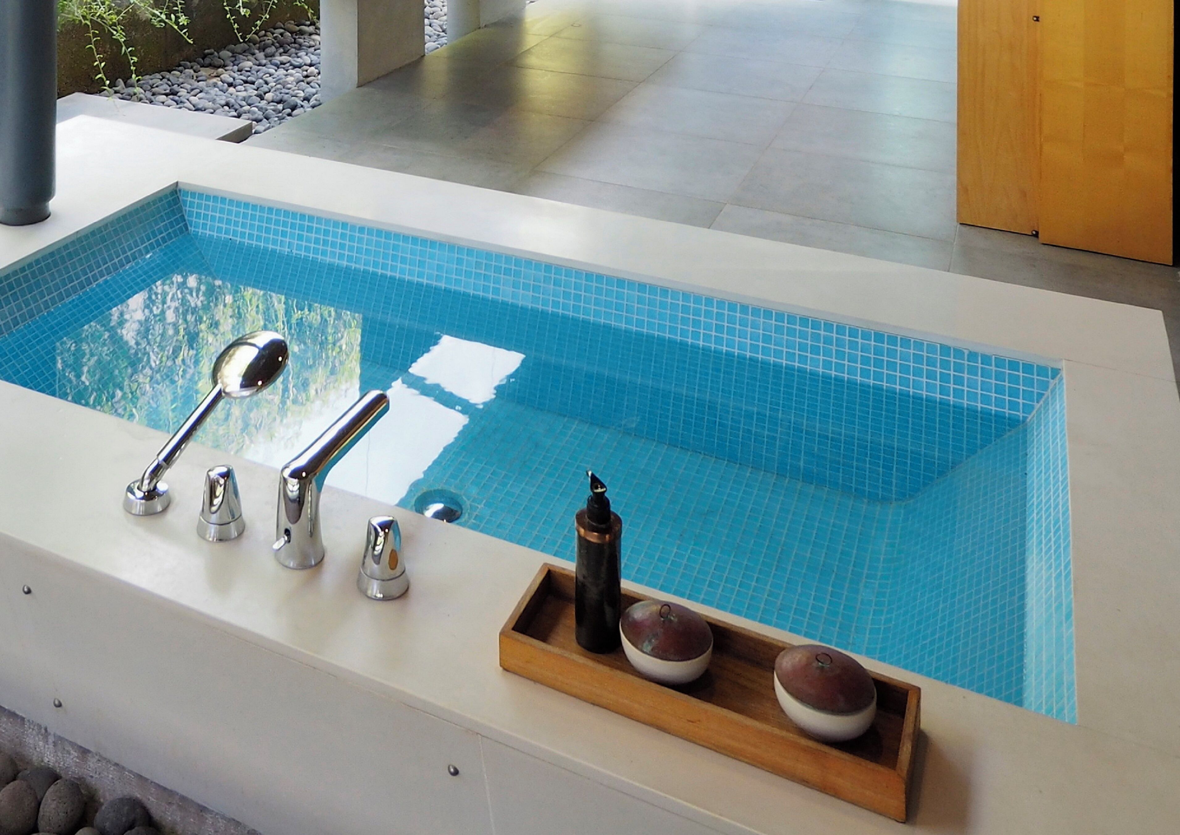 Una piscina interior moderna con forma rectangular, azulejos azules cristalinos y un conjunto de grifos cromados.