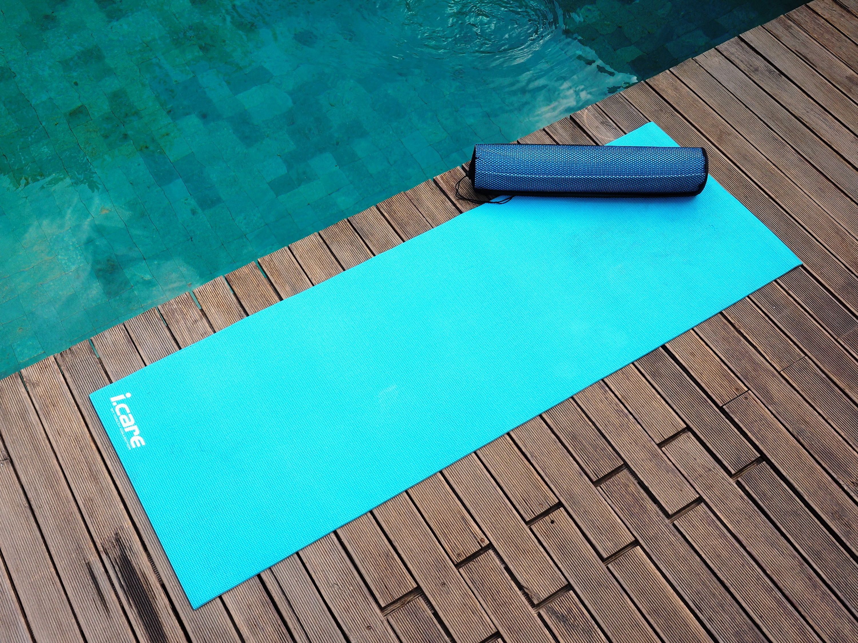 Eine blaue Yogamatte und ein Yoga-Baustein auf einem Holzdeck an einem Pool.
