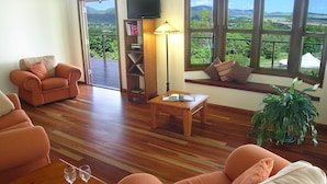 Una sala de estar con un sofá, una mesa de centro y una estantería. Hay un televisor sobre un mueble bajo y una ventana con vistas al exterior.