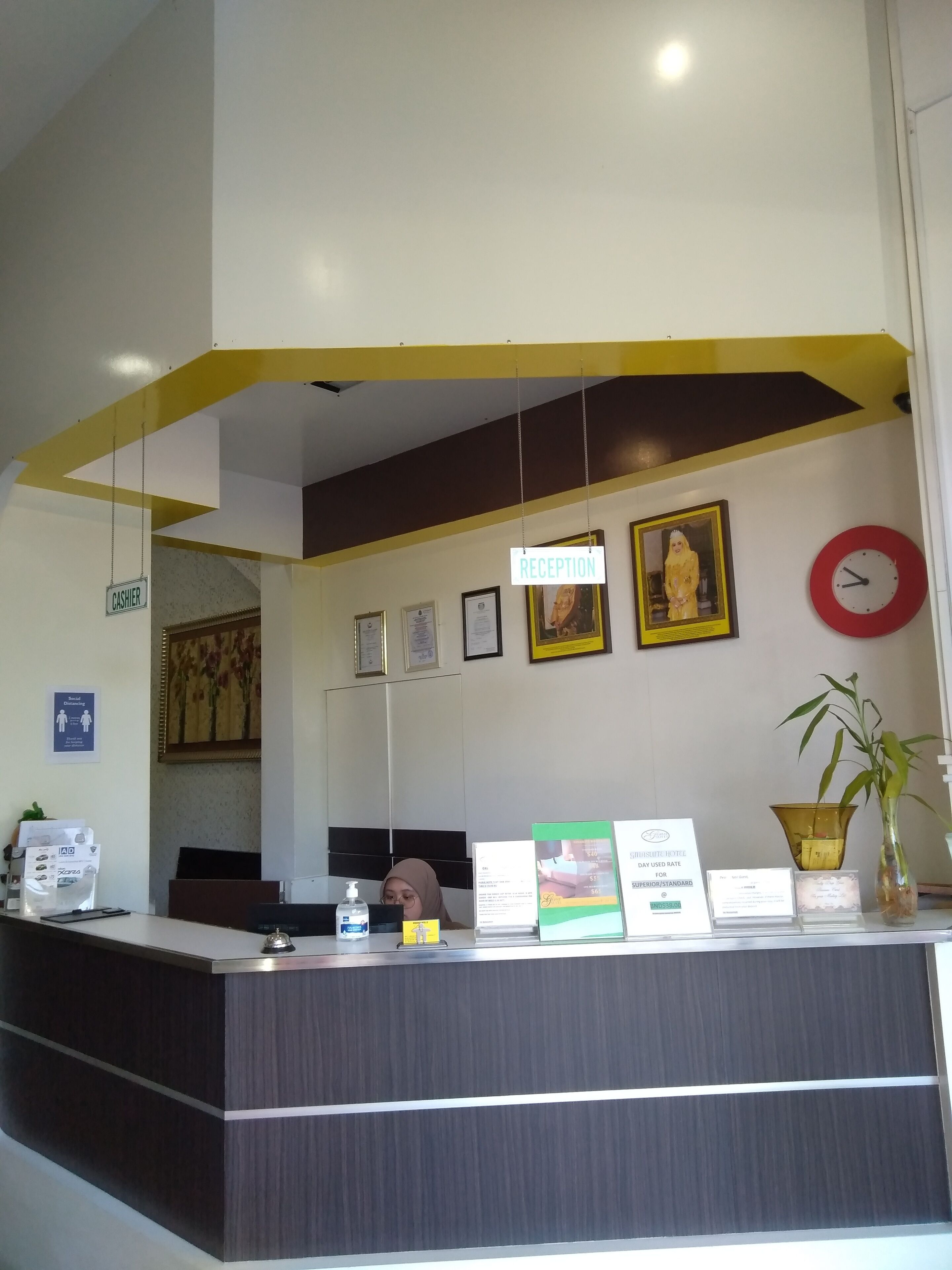 A reception desk with a sign indicating 'RECEPTION', a clock, framed certificates, and a potted plant.