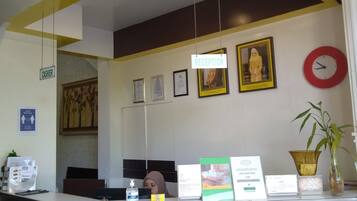 A reception desk with a sign indicating 'RECEPTION', a clock, framed certificates, and a potted plant.