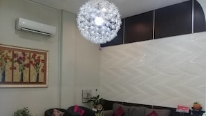 Una sala moderna con un sofá blanco, un sillón negro y una mesa de centro. Hay una lámpara decorativa sobre el sofá y un aire acondicionado de pared.