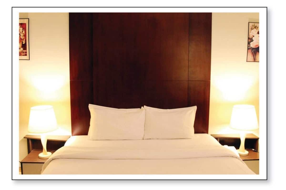 Een hotelkamer met een groot bed, twee bedlampjes en een hoofdeinde van donker hout.