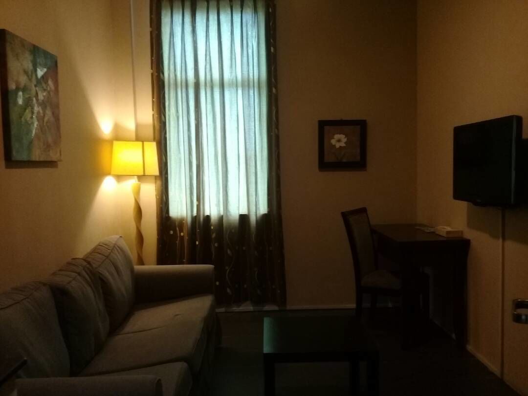 A living room with a sofa, a glass coffee table, a lamp, a TV, and a window with curtains.