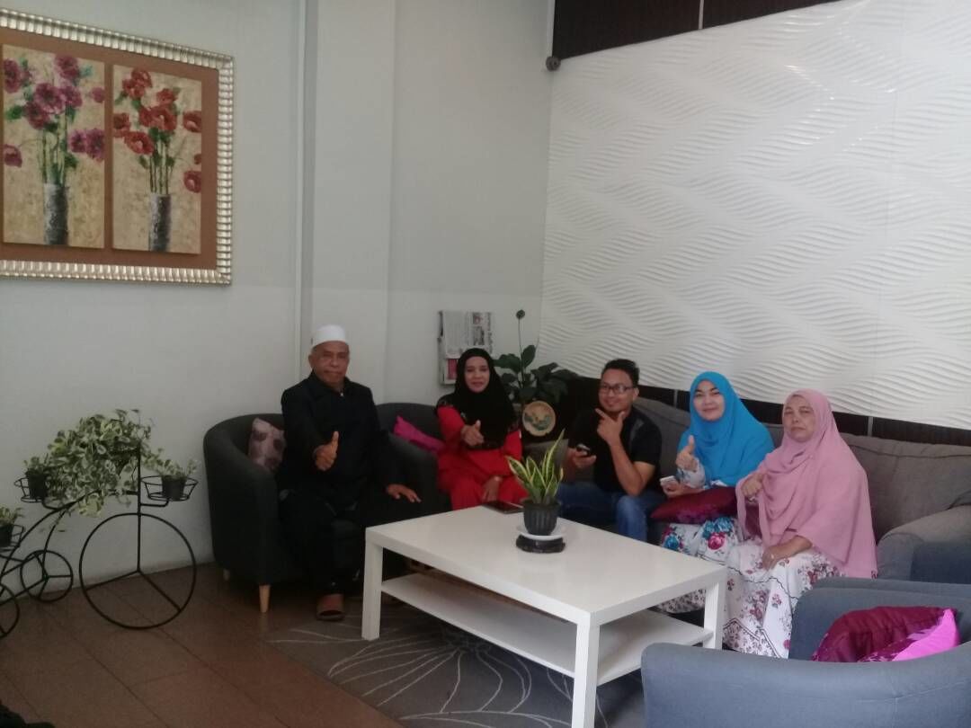 A group of people seated on a couch in a living room with a white coffee table and a potted plant.