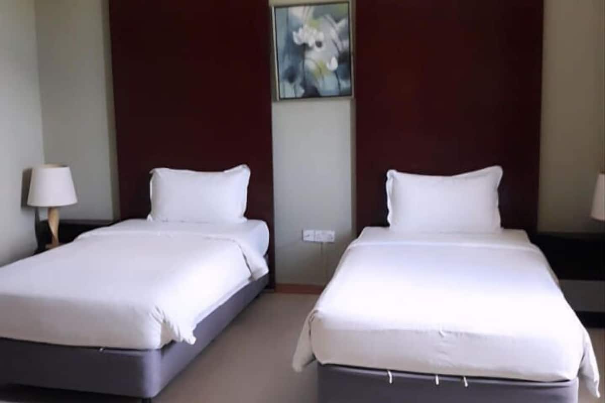 Een hotelkamer met twee bedden, een nachtkastje met een lamp en een schilderij aan de muur.