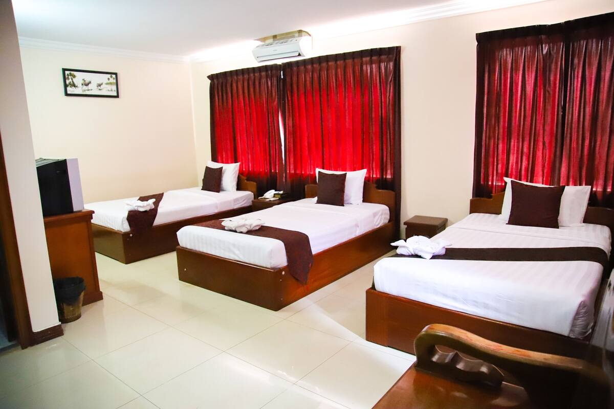 A hotel room with three beds, a TV, and a trash bin.