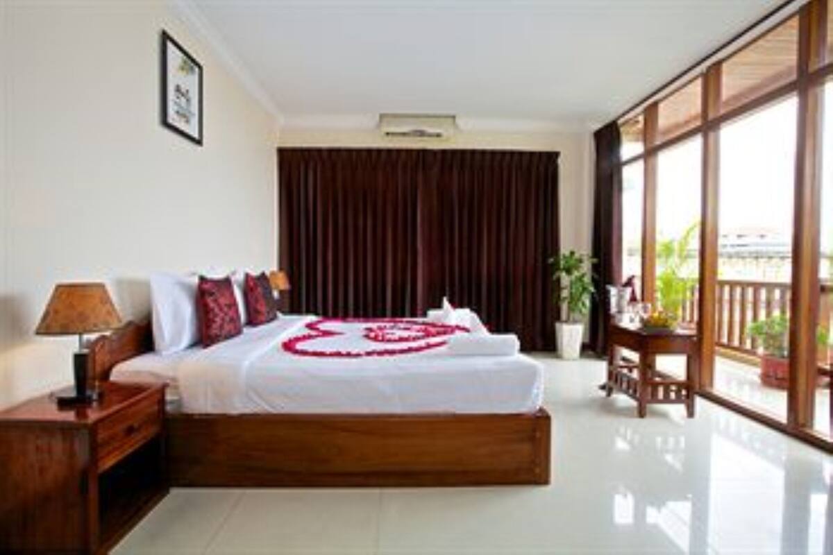 A hotel room with a large bed, a nightstand, a window with a view, and a potted plant.