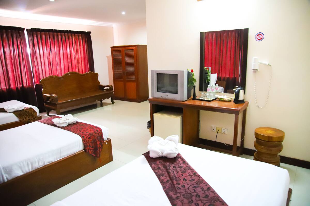 A hotel room with two beds, a wooden wardrobe, a television, a desk with a telephone, and a mirror.