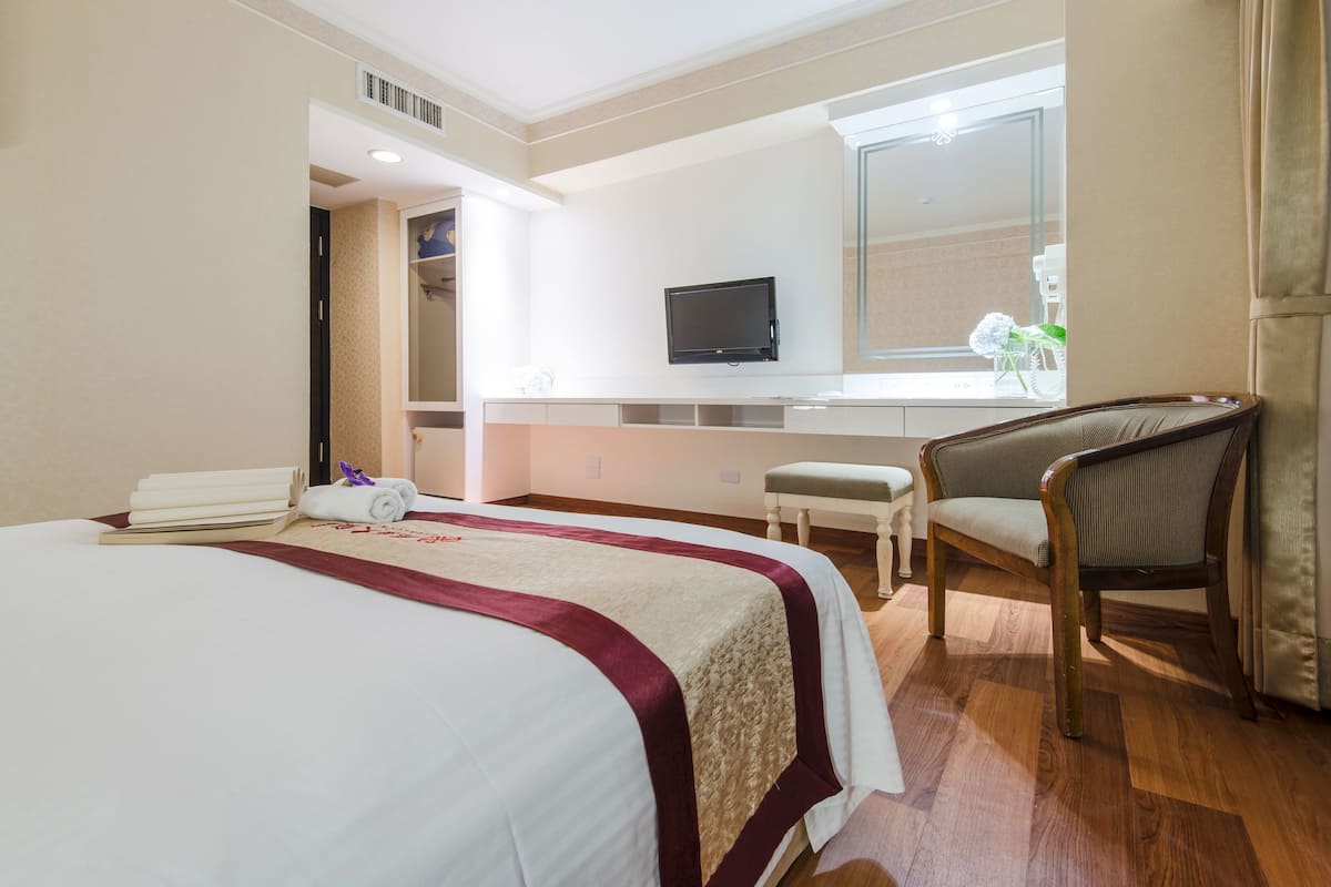 Hotellihuone, jossa on sänky, tuoli, televisio ja pieni pöytä.
