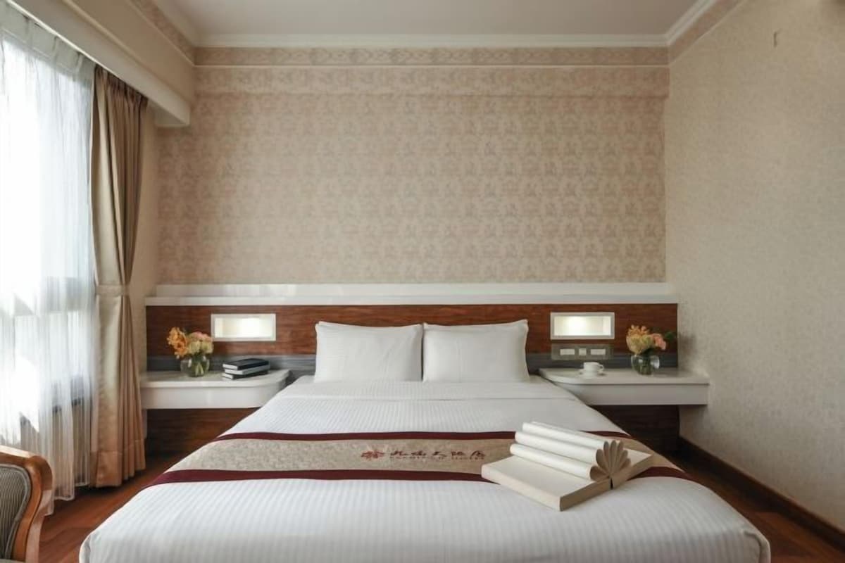 Una habitación de hotel con una cama grande, dos mesitas de noche y un ventanal con cortinas.