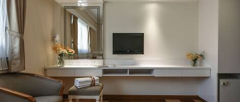 Un baño moderno con tocador, espejo, televisor montado sobre el tocador, una silla y un banco.