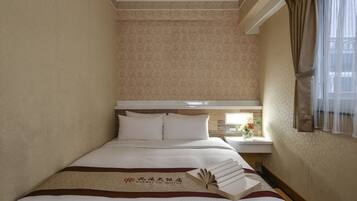 A hotel room with a neatly made bed, a bedside table with a vase of flowers, and a window with curtains.