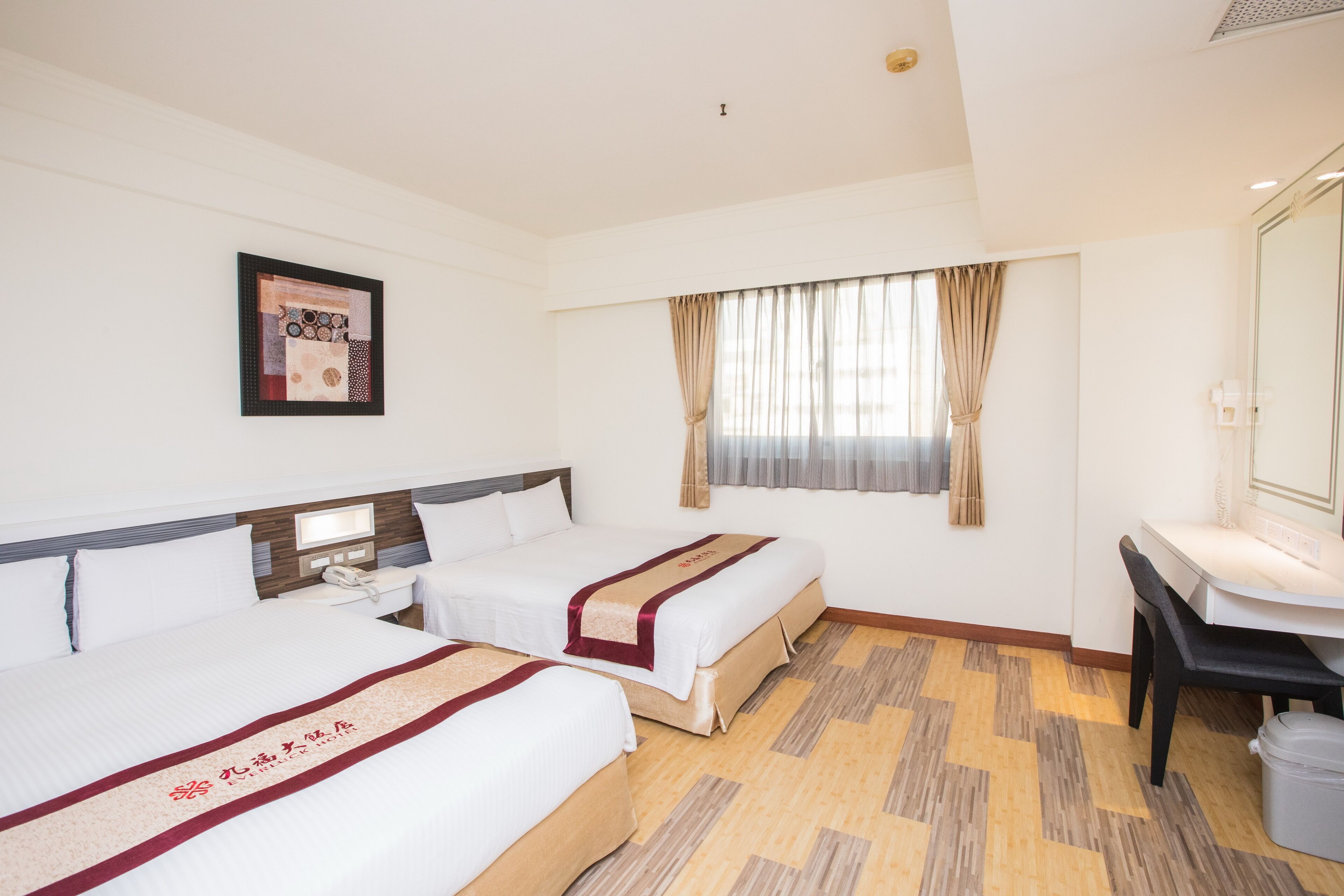 Une chambre d’hôtel avec deux lits, un bureau, une chaise, un téléphone et une fenêtre avec des rideaux.