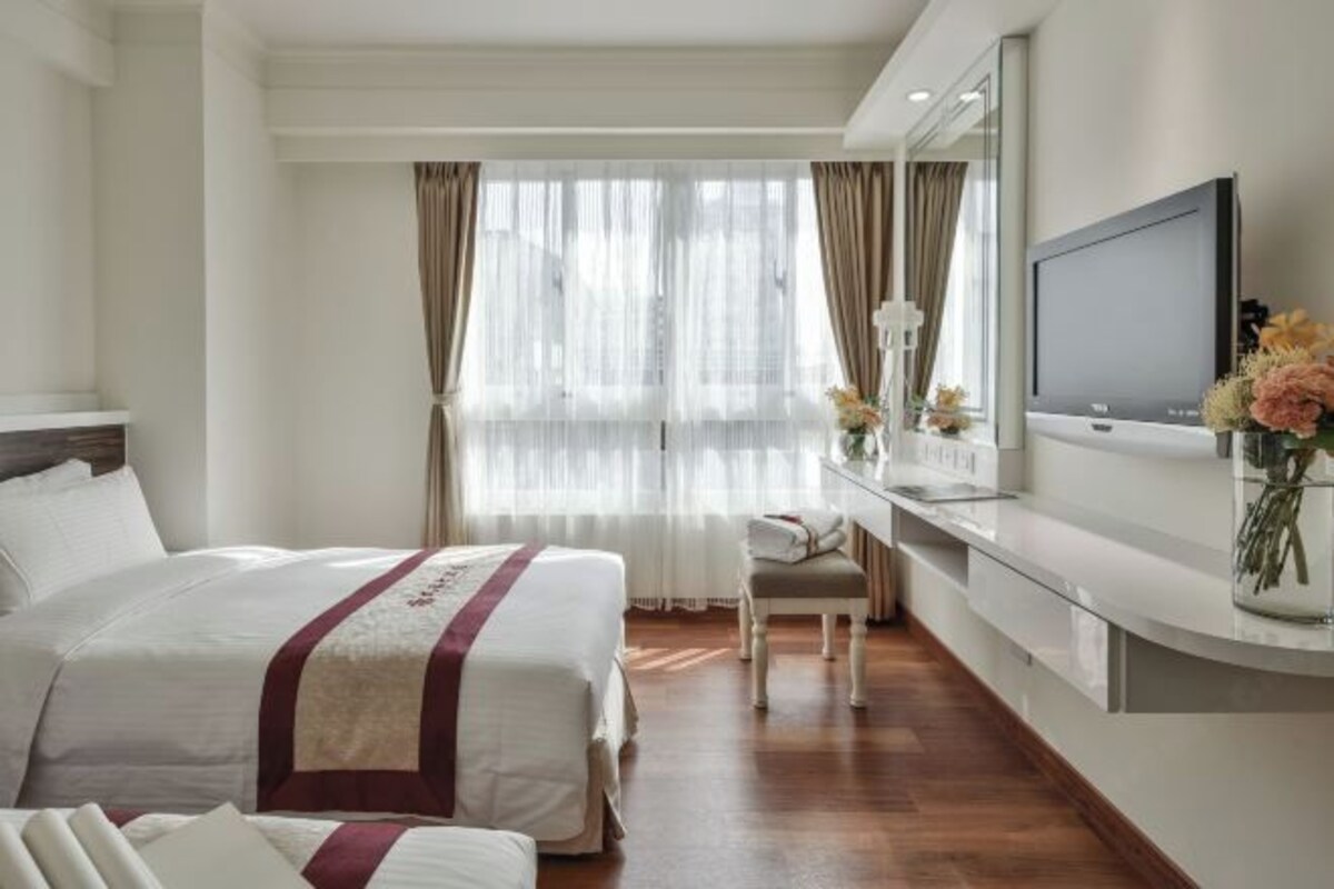 A hotel room with a large bed, a desk, a television, and a vase with flowers.