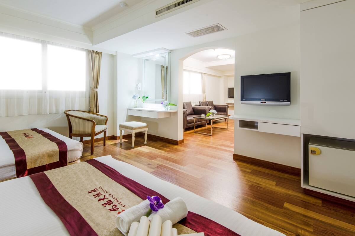 Hotellihuone, jossa on kaksi sänkyä, työpöytä, tuoli, televisio ja näkymä oleskelutilaan.