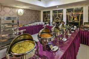 A buffet setup with multiple food stations, including a variety of dishes in large metal containers, arranged on a table with a purple tablecloth. - Harmonious Hotel (Kaohsiung)