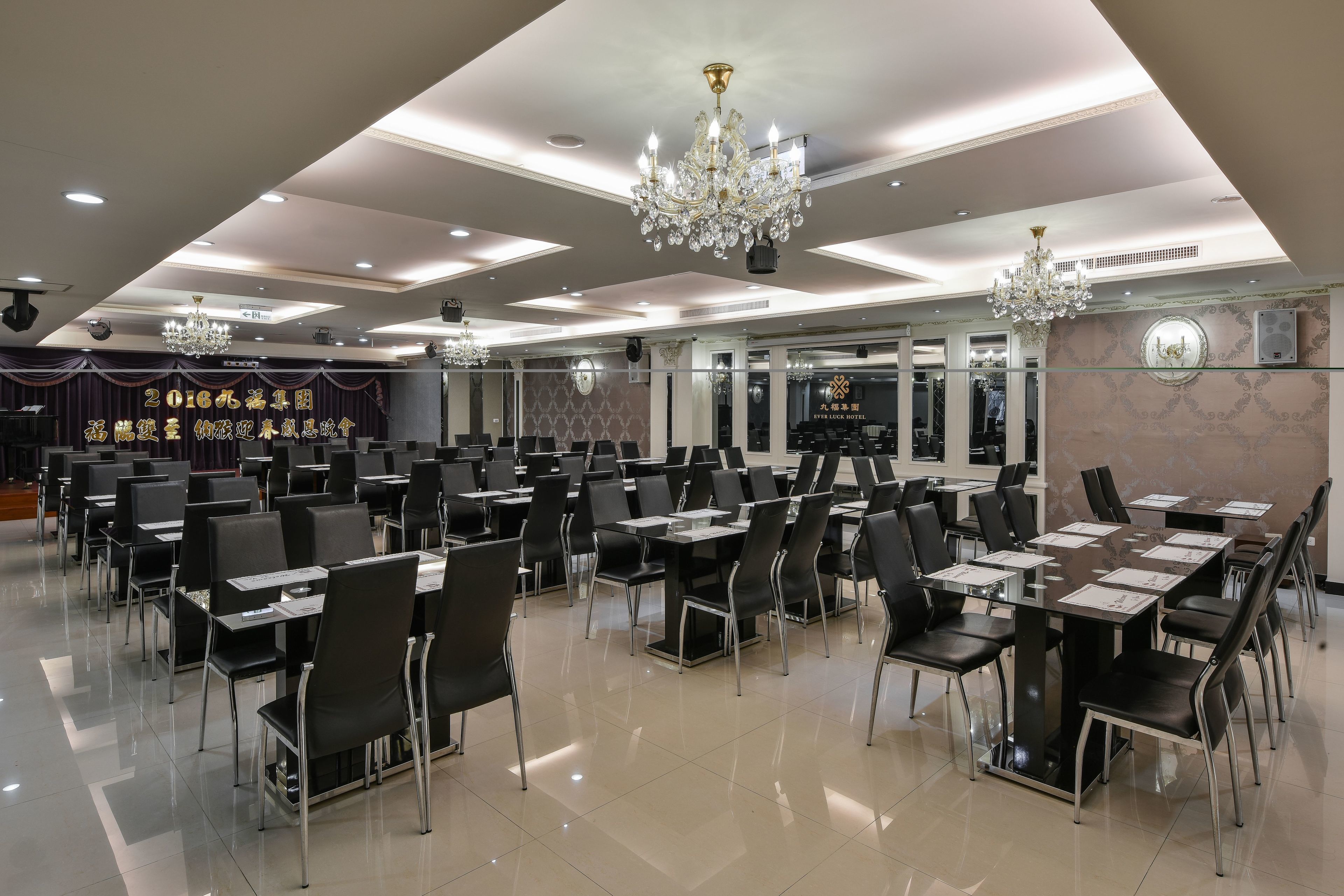 A conference room with tables and chairs, chandeliers, and a stage with curtains.