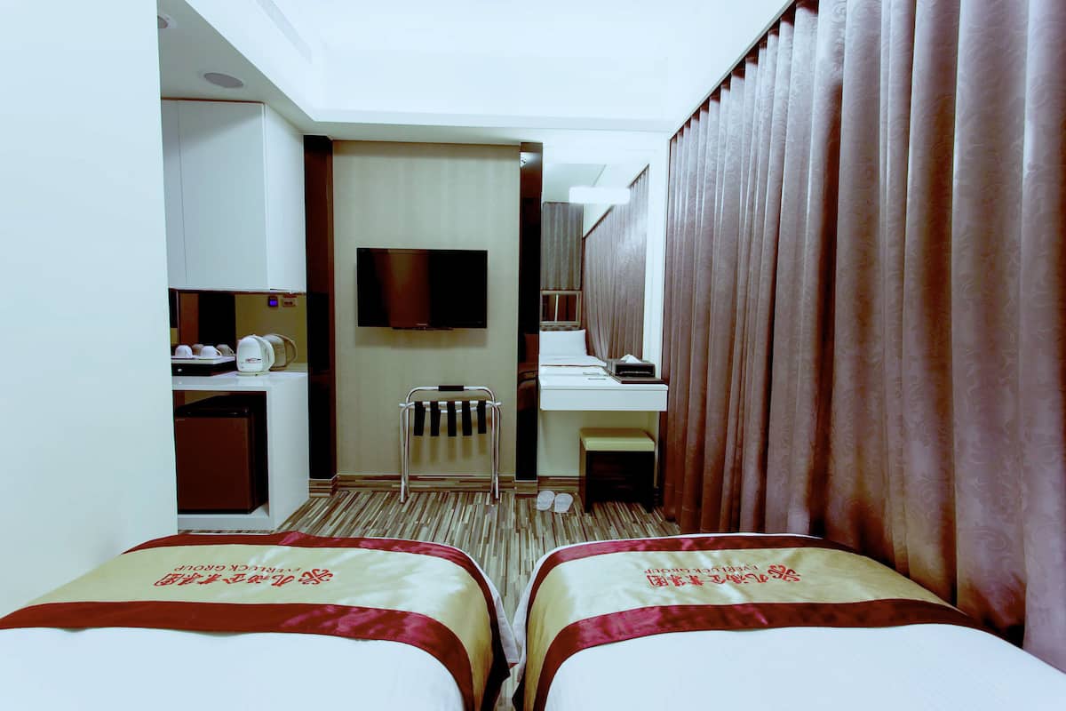 Une chambre d’hôtel avec deux lits, une télévision, un bureau avec un ordinateur, un petit réfrigérateur et une salle de bain avec un rideau de douche.