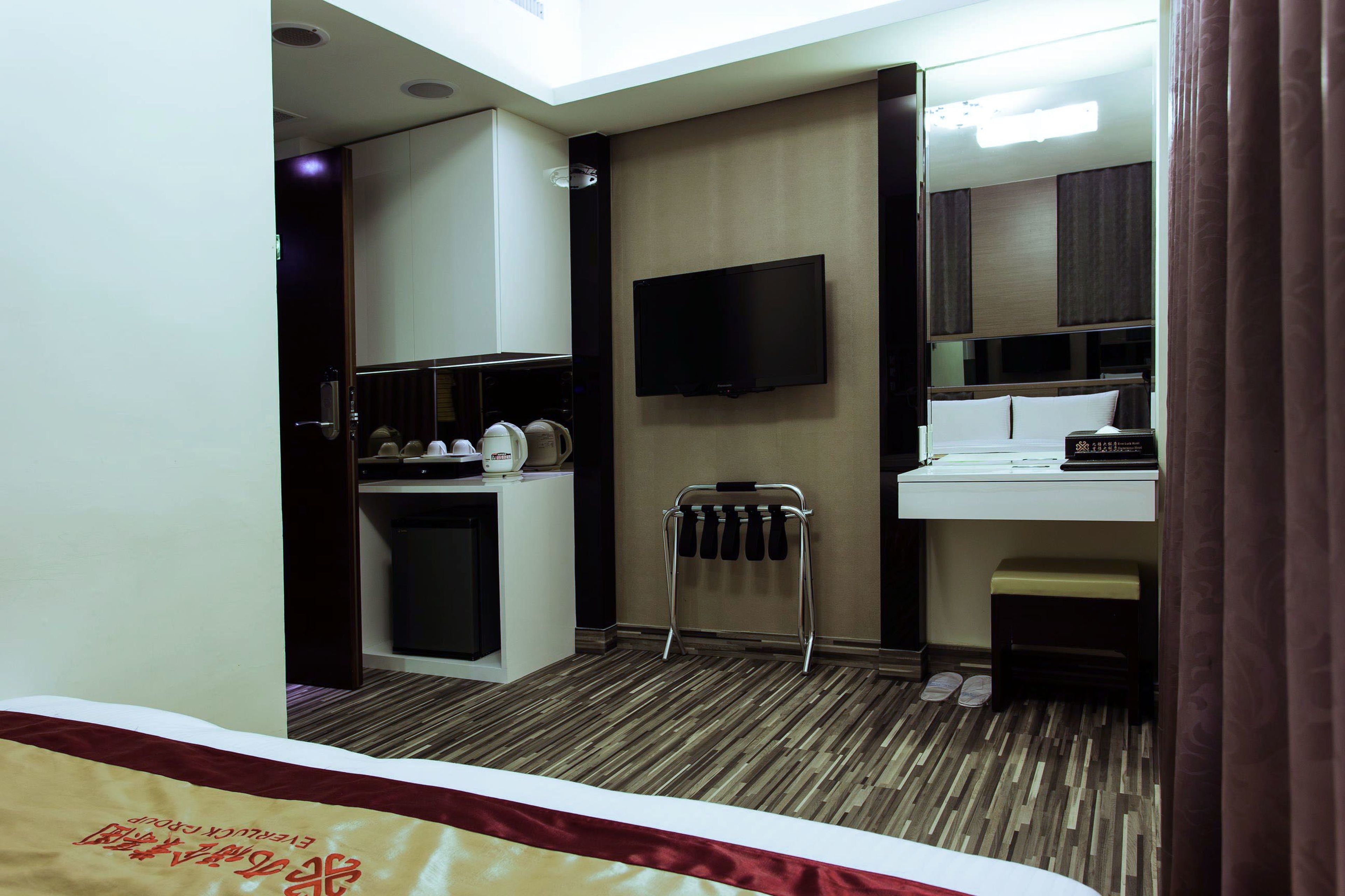 A hotel room with a bed, a small kitchenette, a television, and a mirror.