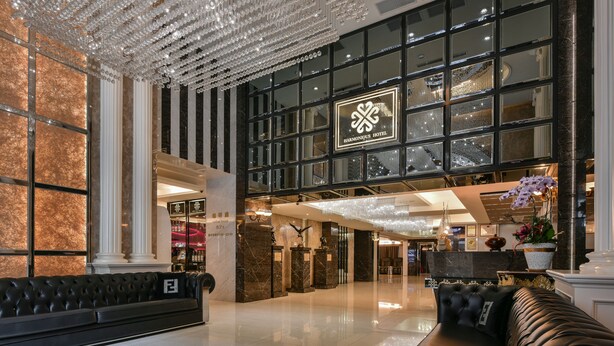 A spacious lobby with a black leather sofa, a chandelier, and a large window with the Harmonious Hotel sign. - Harmonious Hotel (Kaohsiung)