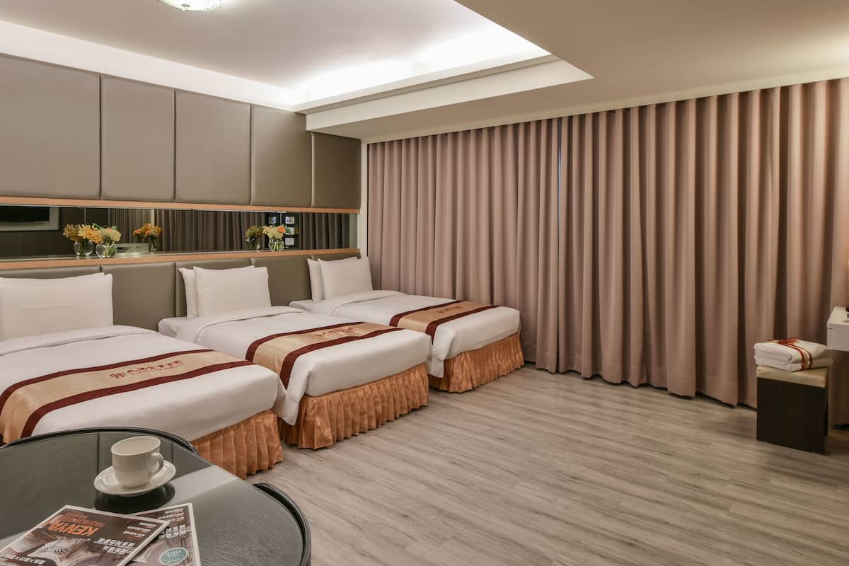 Une chambre d’hôtel avec deux lits, une petite table sur laquelle se trouvent une tasse et un magazine, un miroir et une grande fenêtre avec des rideaux.