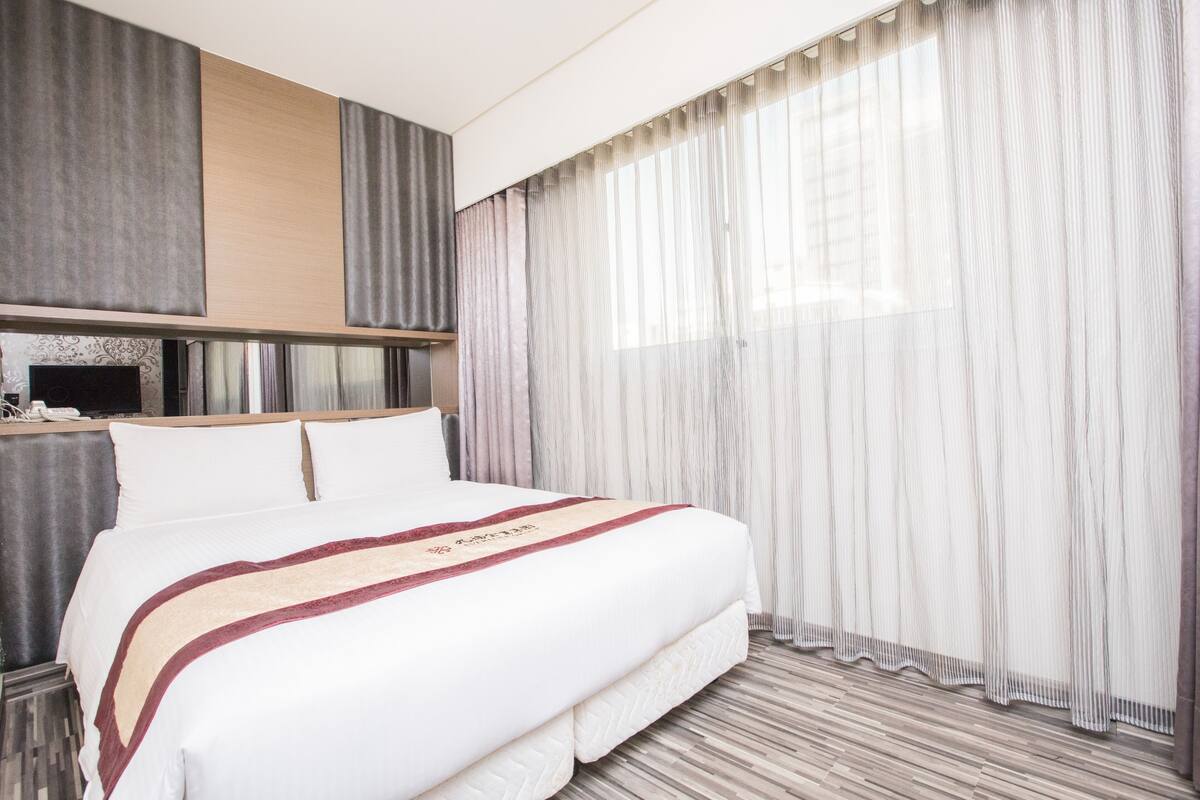 Une chambre d’hôtel avec un grand lit, un téléviseur à écran plat et des rideaux en voile.