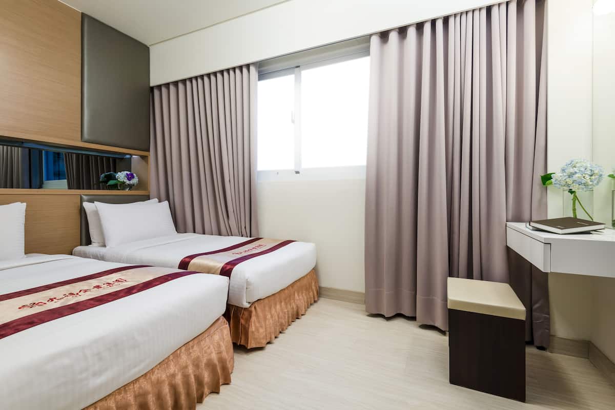 Une chambre d’hôtel avec deux lits, un bureau et une fenêtre avec des rideaux.