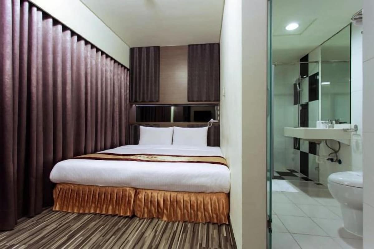 A hotel room with a large bed, a glass shower enclosure, and a separate bathroom with a sink and toilet.