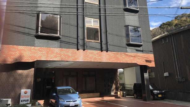Een meerhoog gebouw met een parkeergarage-ingang, een BizHotel bord en een blauwe auto die in de garage staat.