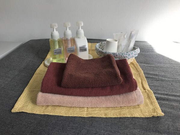 A bathroom setup with a towel rack holding a folded towel, a bottle of shampoo, a bottle of body soap, a bottle of conditioner, and a cup. - Biz Hotel Kiiyura (Yura)